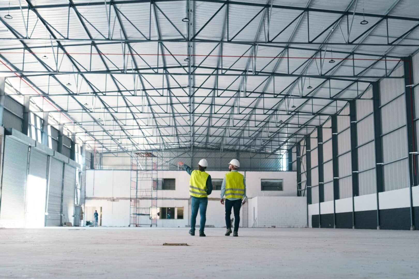Construction workers inspecting large, empty warehouse interior.