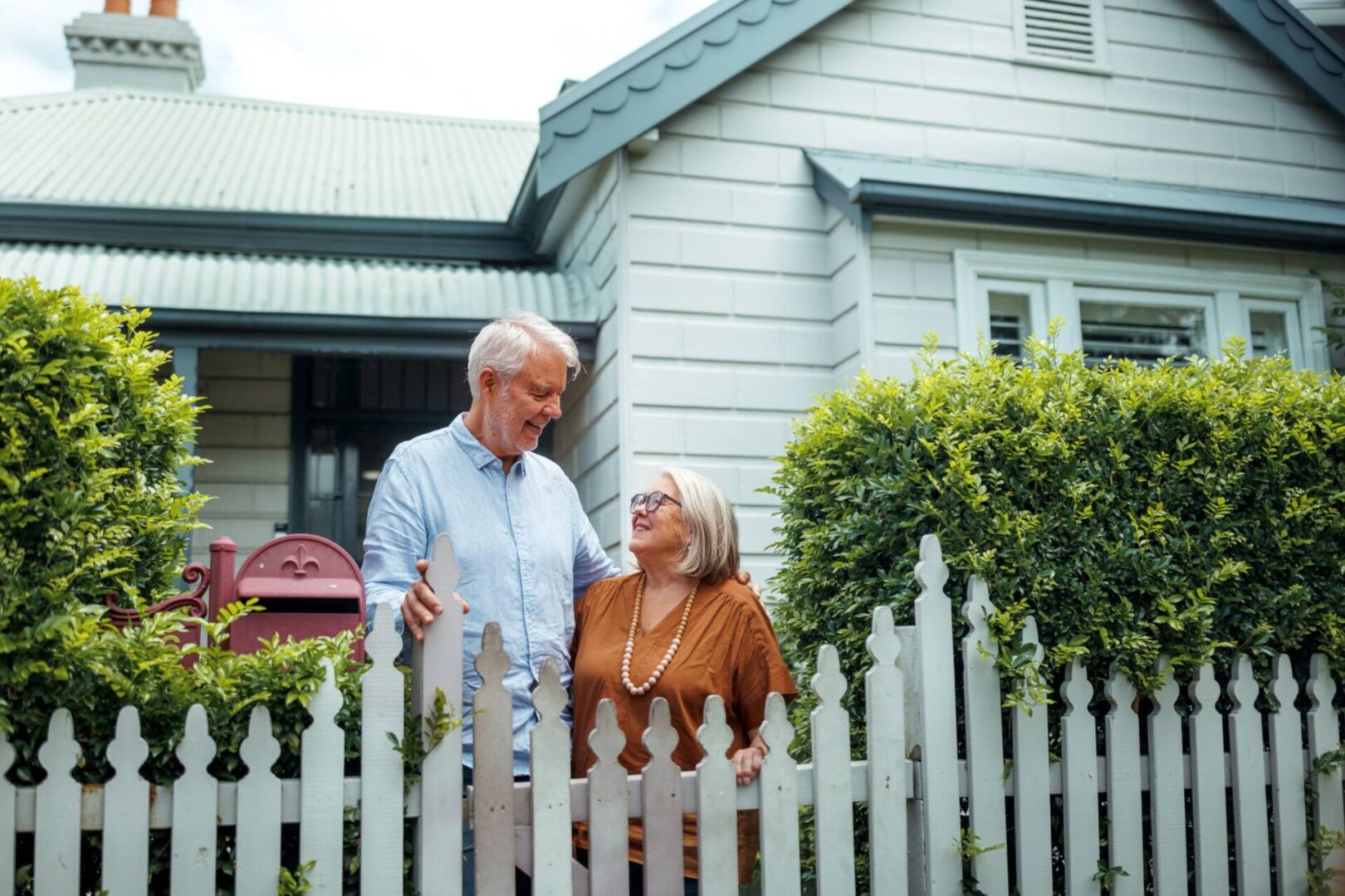 Elderly couple smiling outside their house.